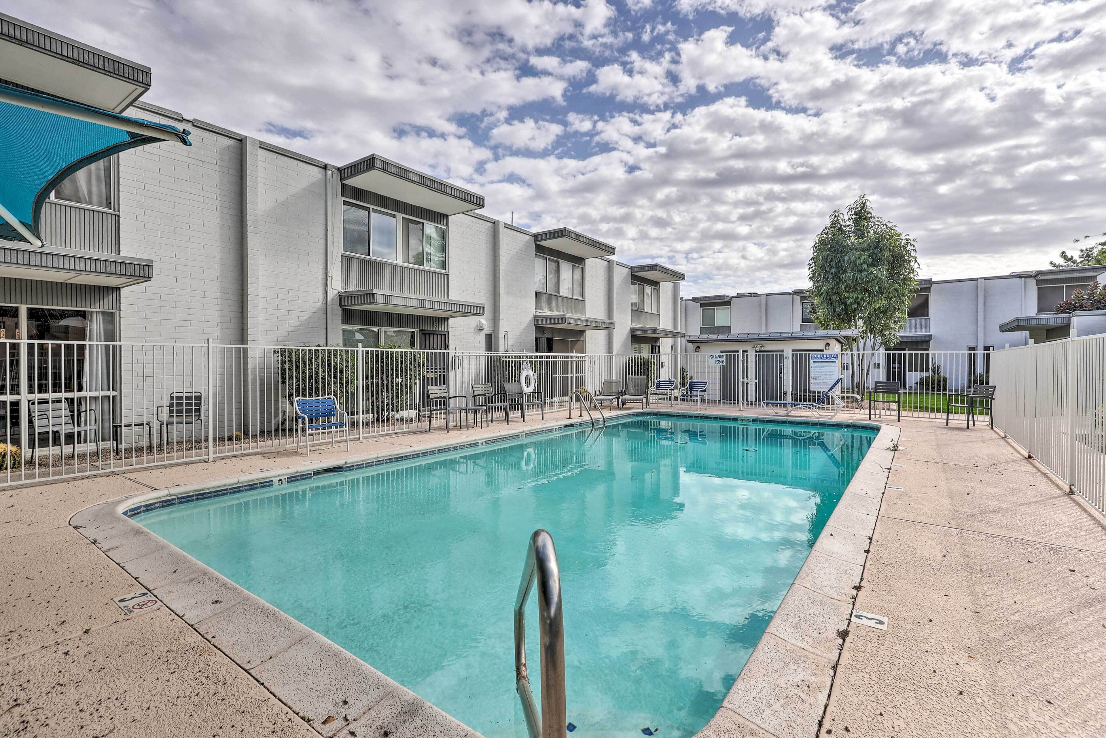 A swimming pool with a metal ladder, surrounded by a white fence and lounge chairs.