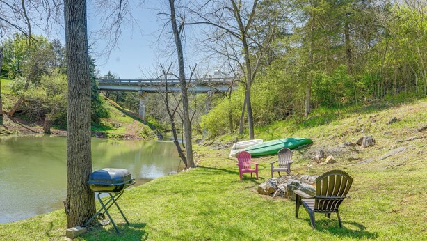 A grassy area with a grill, chairs, and a canoe by a river.