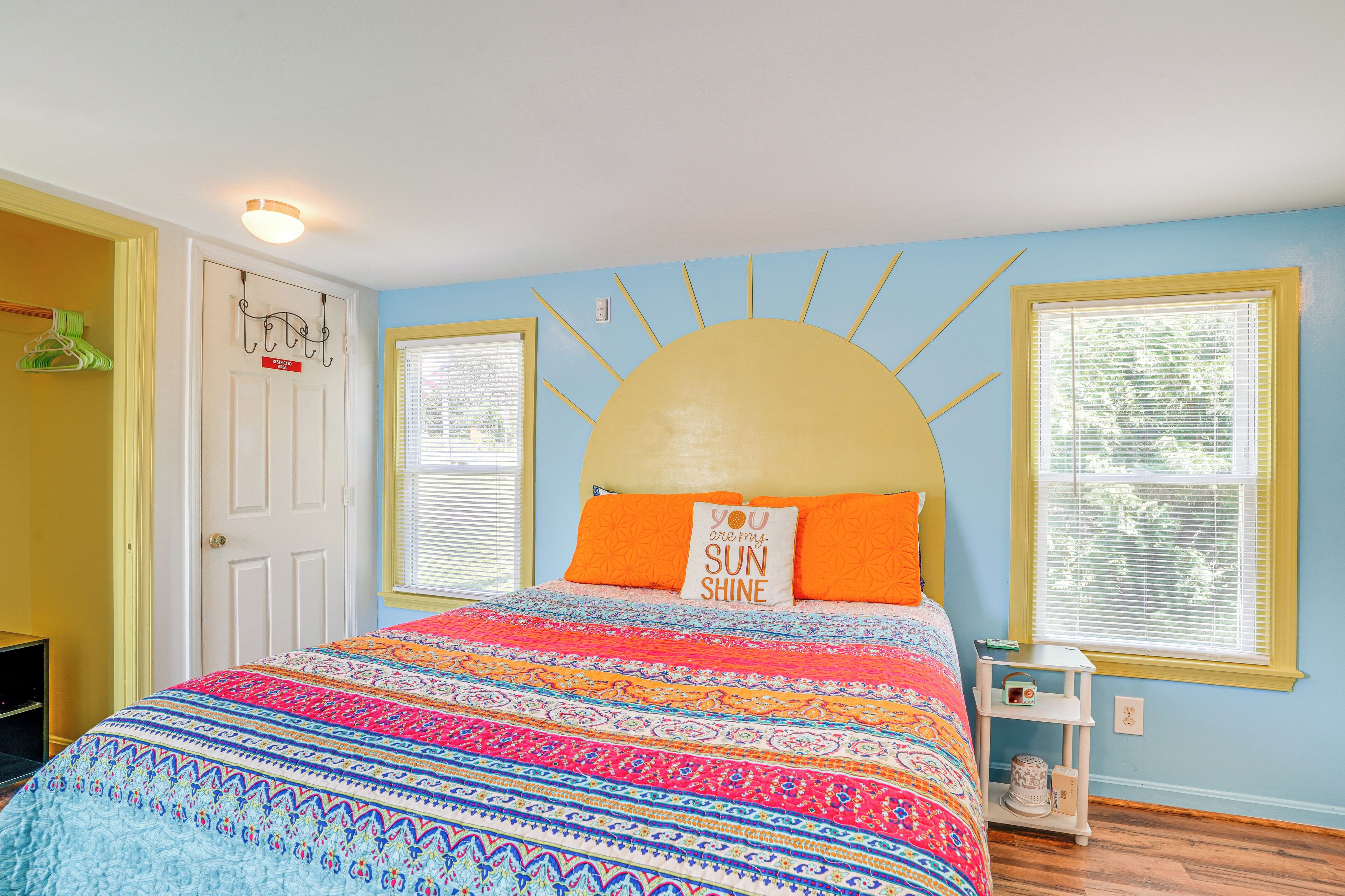 A bedroom with a bed, a sun-shaped headboard, a colorful bedspread, and a window with blinds.
