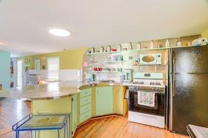 Uma cozinha com ilha central, fogão, geladeira e diversos eletrodomésticos.