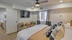 Une chambre à coucher avec un lit, un ventilateur de plafond, un téléviseur fixé au mur et une fenêtre avec des rideaux.