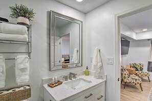Un baño con lavamanos blanco, un espejo grande y un perchero para toallas.