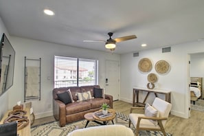 Un salon avec un canapé en cuir marron, un fauteuil blanc, une table basse en bois et un ventilateur de plafond.