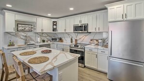 Une cuisine moderne avec des meubles blancs, un îlot central, des appareils en acier inoxydable et un pare-feu en marbre.