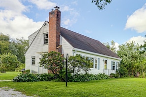 A single-story house with a brick chimney, white siding, and a dark roof. - Hampton 'quiet Corner Cottage' w/ Fireplace & Yard (Hampton)