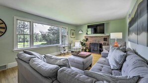 Una sala de estar con un sofá gris, una chimenea y un ventanal grande.