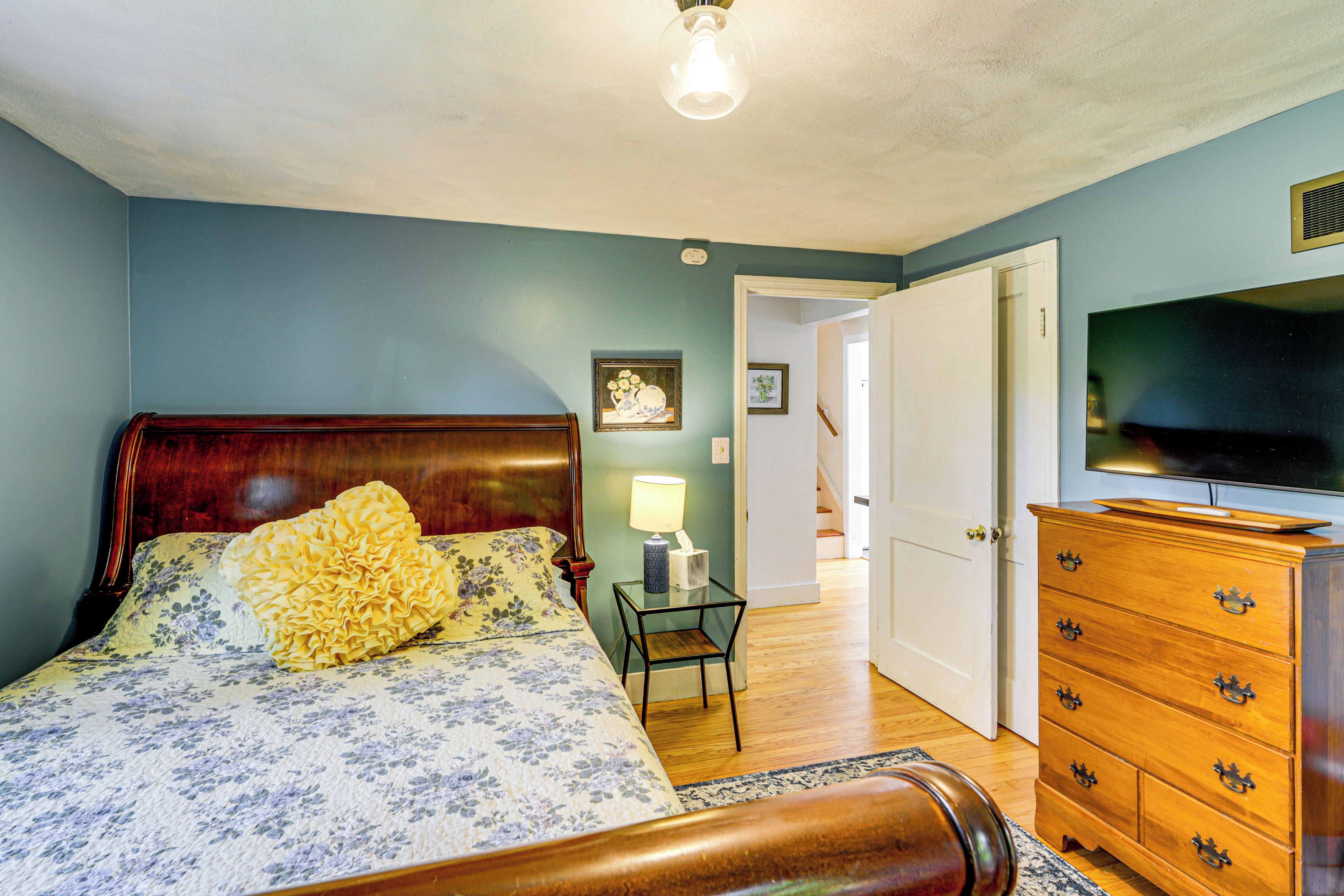 A bedroom with a bed, dresser, television, and a door leading to another room.