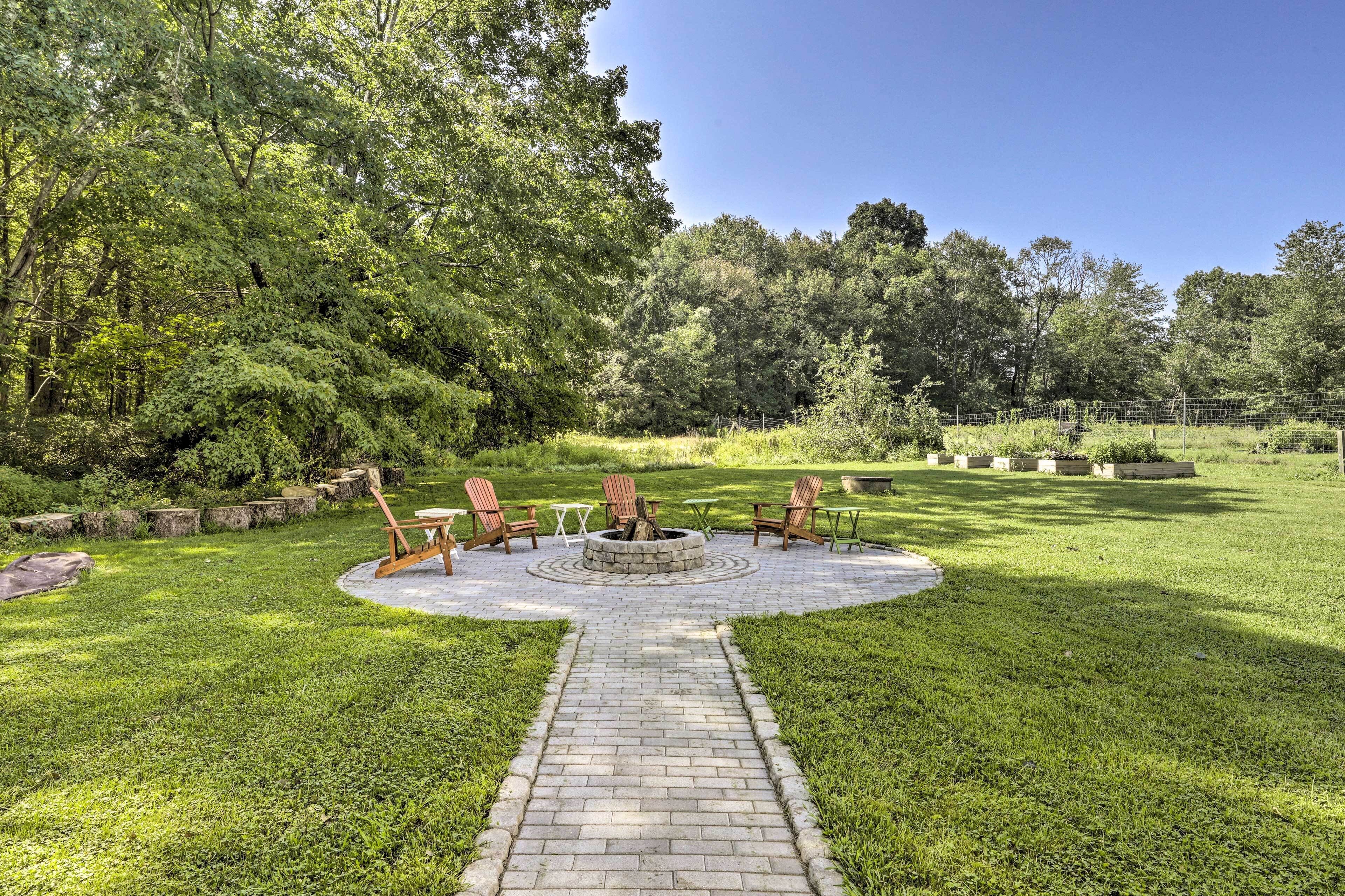 A circular outdoor seating area with a fire pit, surrounded by a brick pathway, and a grassy lawn with trees in the background.
