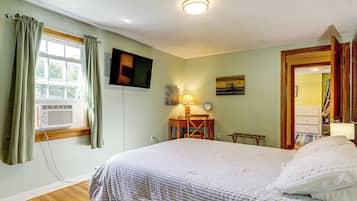 A bedroom with a bed, a desk, a chair, a television, and a window with curtains.