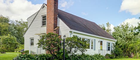 A single-story house with a brick chimney, white siding, and a dark roof.