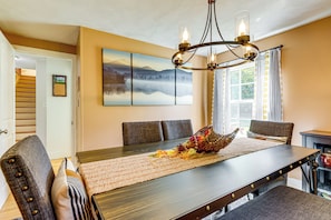A dining area with a wooden table, cushioned chairs, a chandelier, and a large landscape painting on the wall. - Hampton 'quiet Corner Cottage' w/ Fireplace & Yard (Hampton)