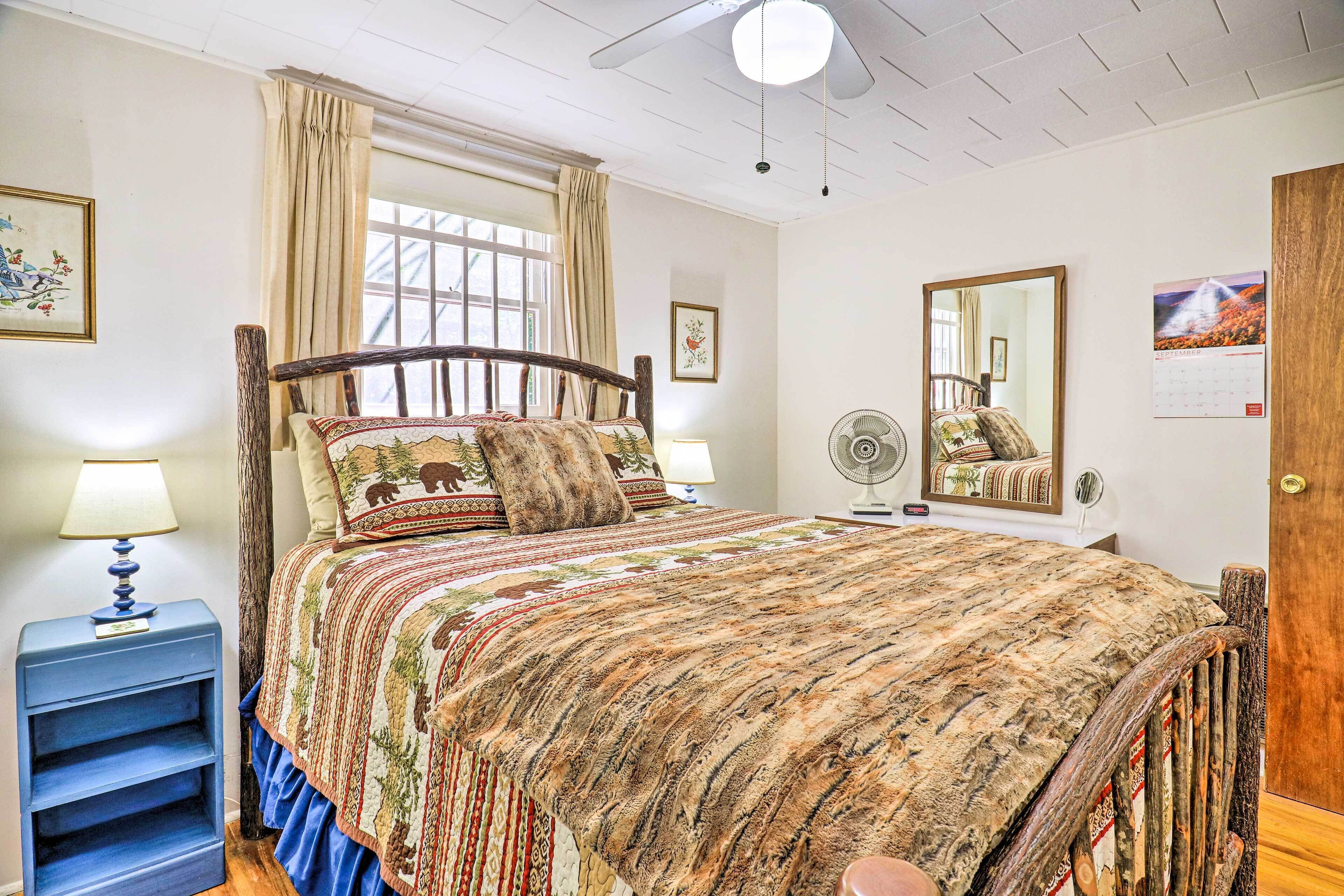 A bedroom with a large bed, a wooden headboard, a nightstand with a lamp, a mirror, and a calendar on the wall.