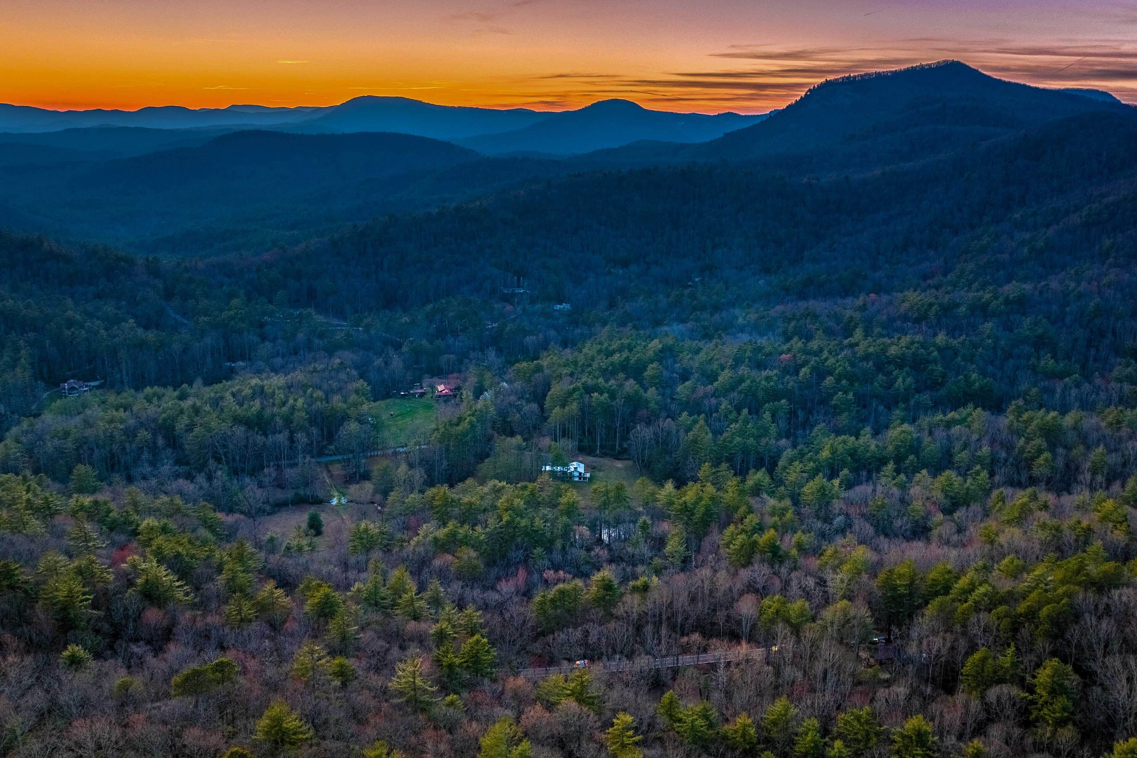 Un paysage montagneux avec une maison entourée d’une forêt dense.