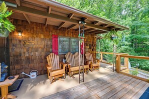 A wooden deck with Adirondack chairs, a welcome sign, and a view of the forest.