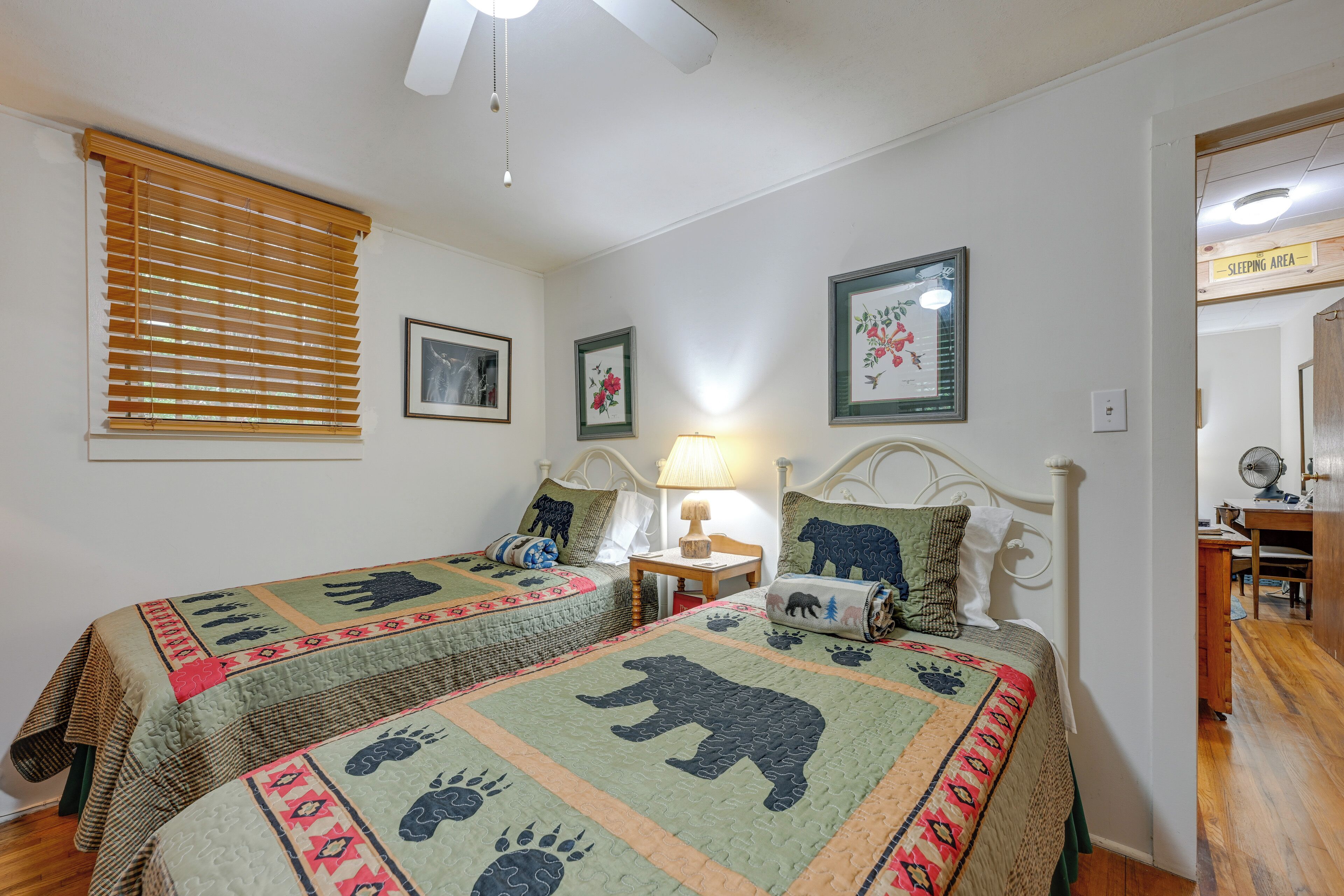 A bedroom with two beds, a ceiling fan, a nightstand with a lamp, and a sign indicating a sleeping area.