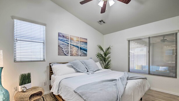 Een slaapkamer met een bed, een plafondventilator, een wandklok en een raam met jaloezieën.