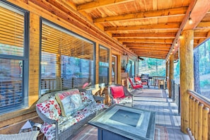 A wooden deck with a sofa and chairs, large windows, and a fire pit.