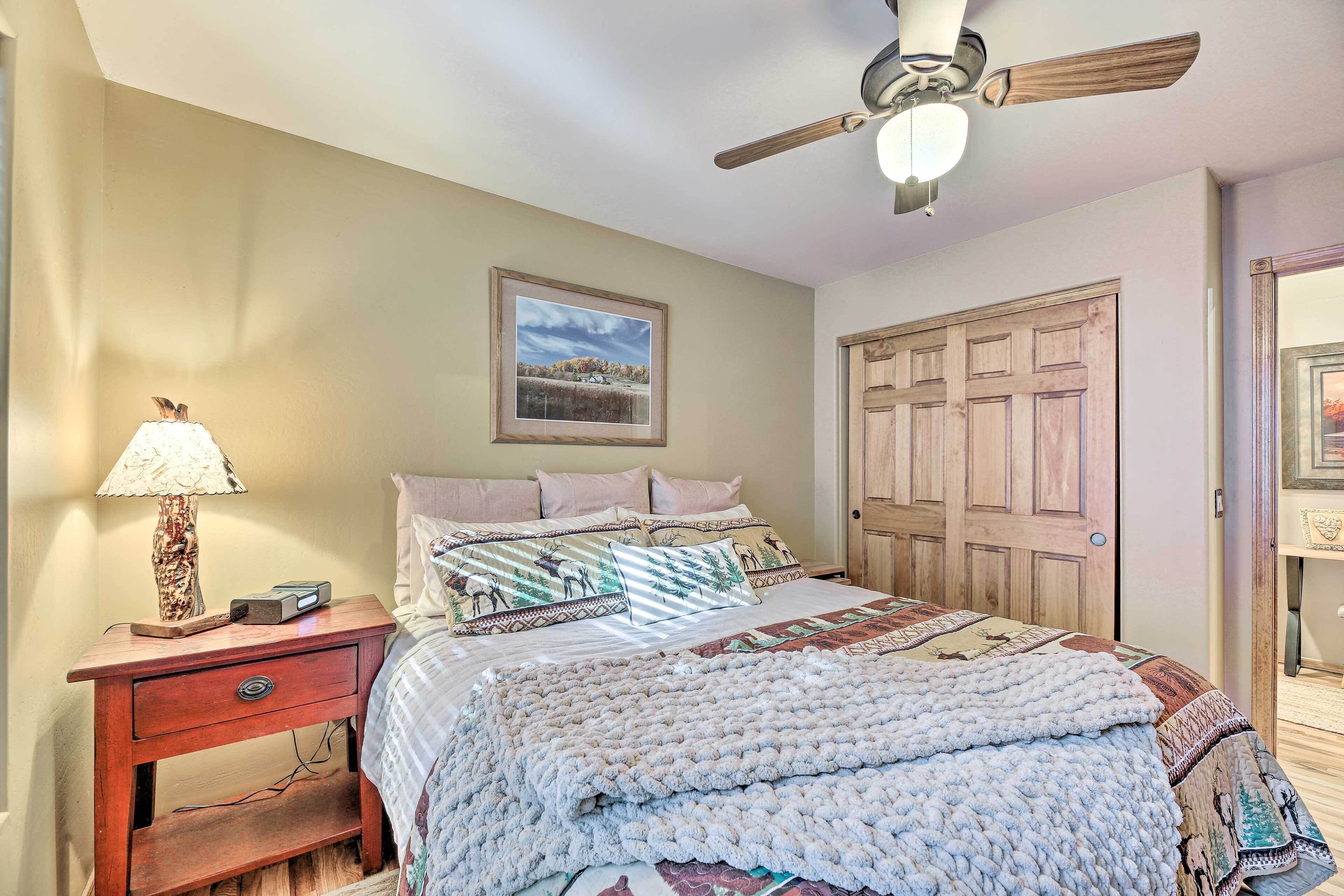 A bedroom with a bed, a nightstand, a lamp, a ceiling fan, and a door.