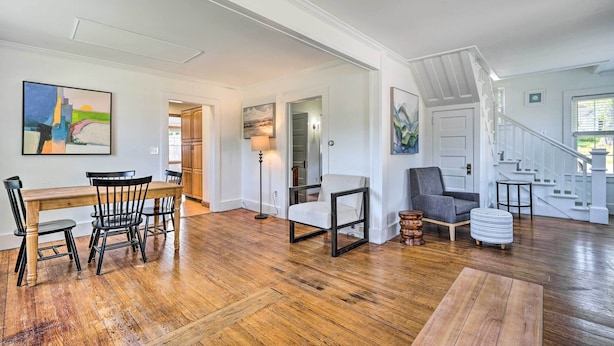 A spacious living room with hardwood flooring, a dining area with a wooden table and chairs, and a staircase leading to an upper level. - Walk to Lake George: Family Escape w/ Game Room! (Lake George)