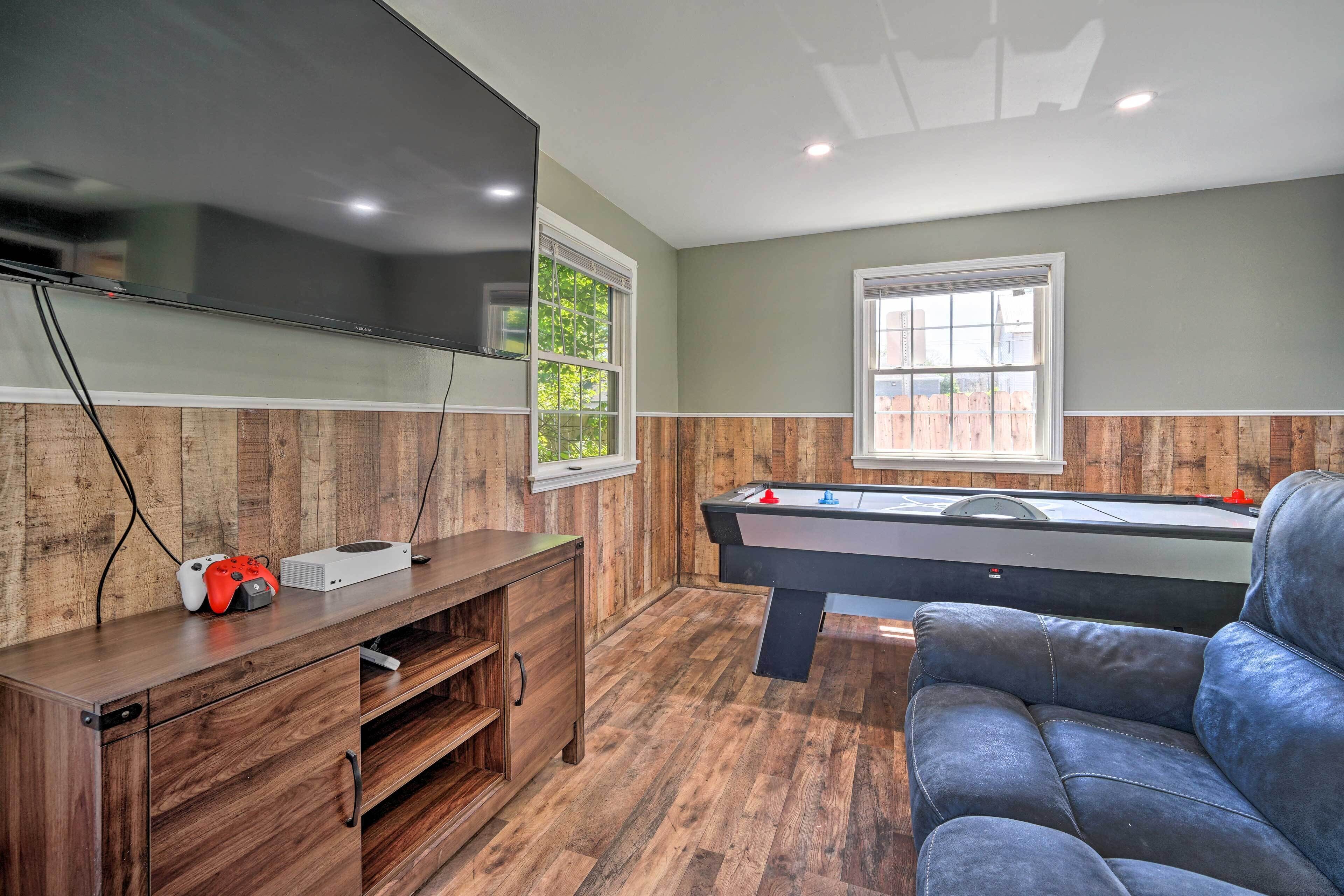 A room with a pool table, a sofa, a TV, and wooden paneling.