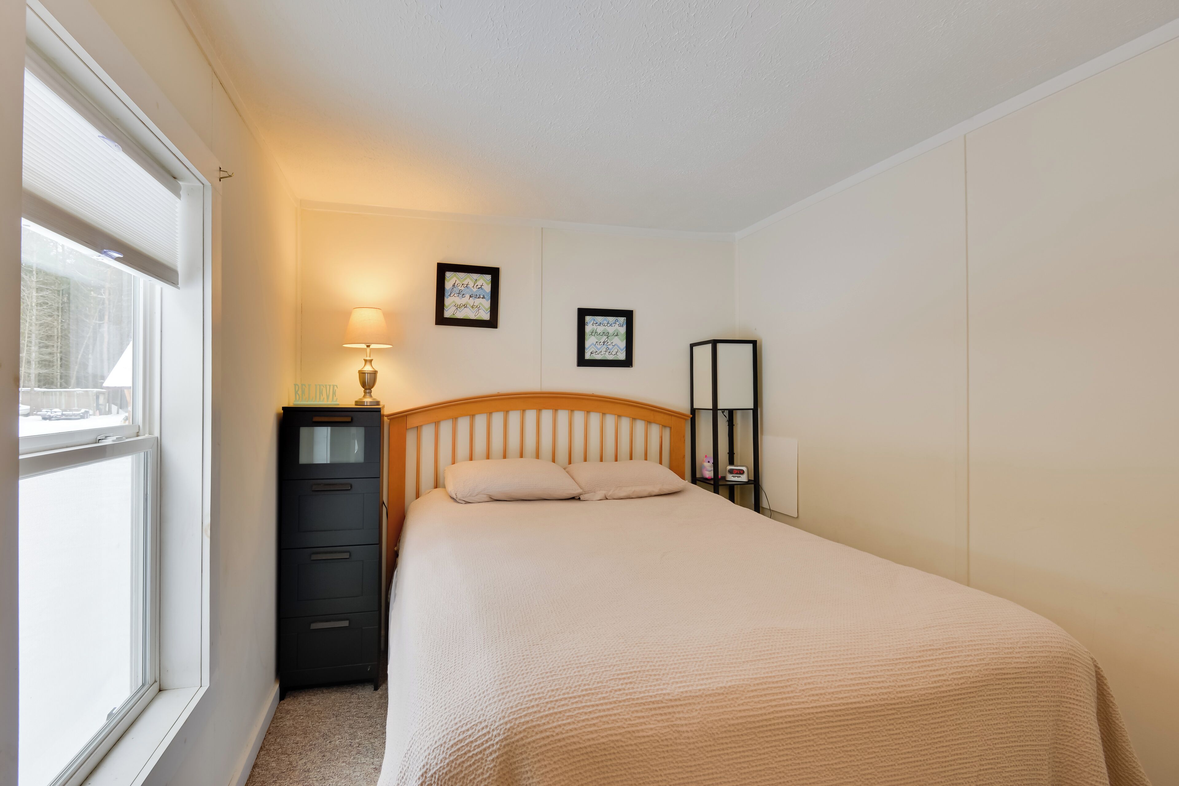 A bedroom with a bed, a nightstand, a lamp, and a dresser.