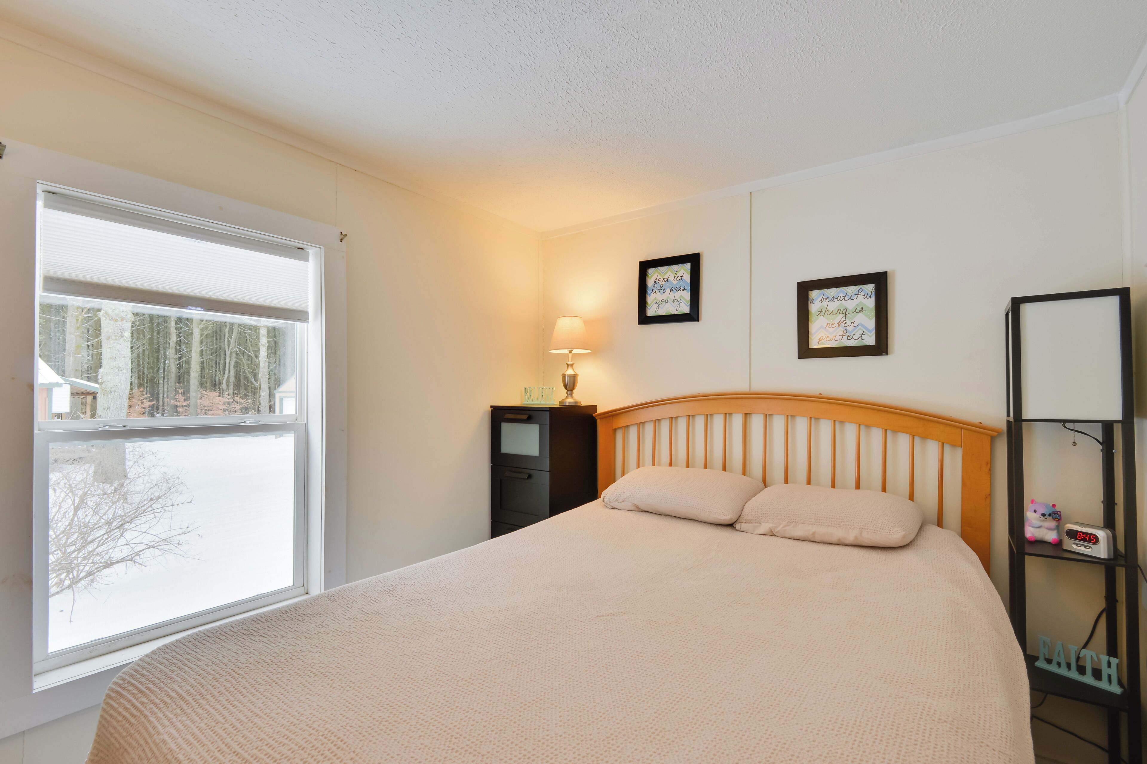 A bedroom with a bed, a nightstand, a lamp, and a wall with two framed pictures.