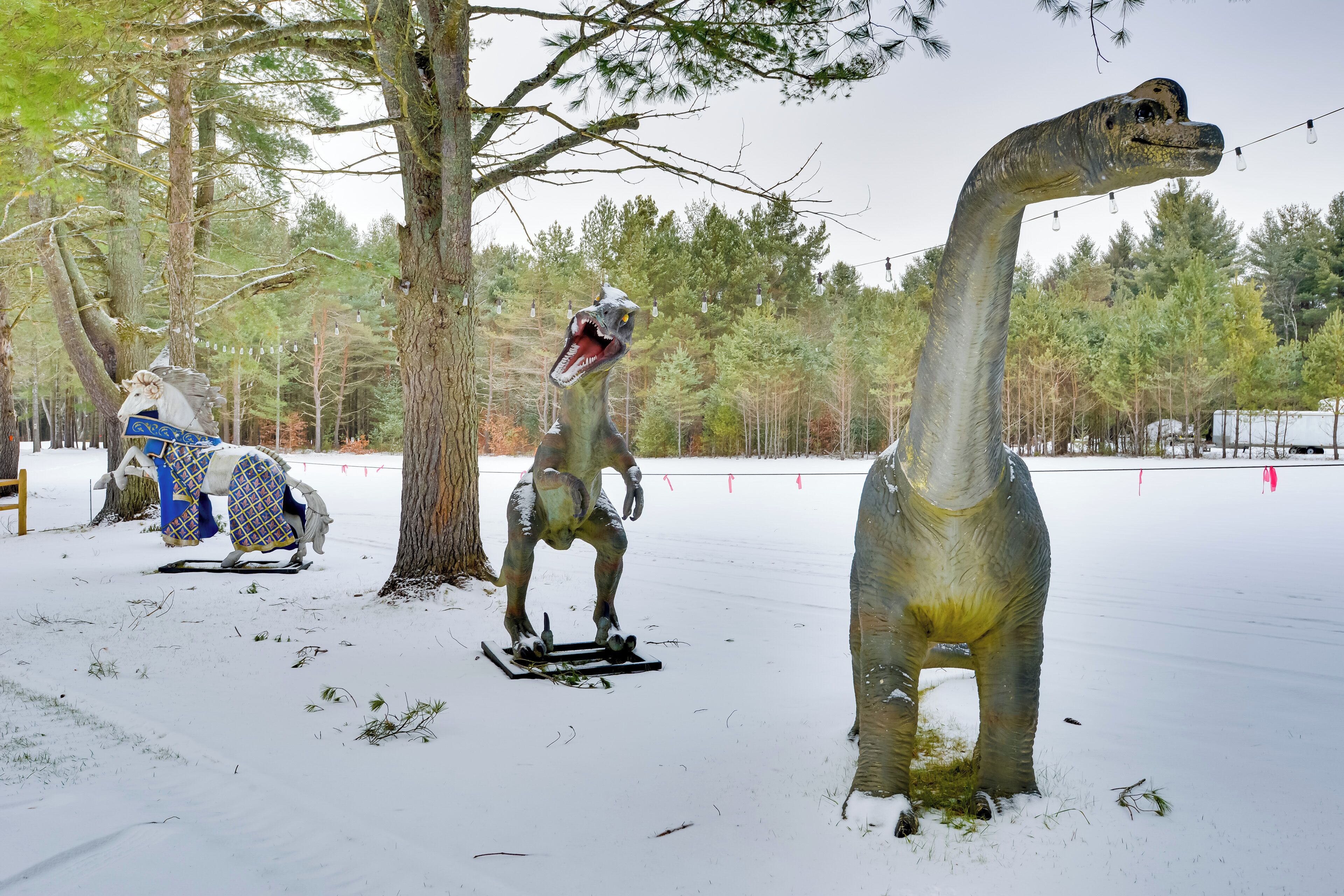 Trois statues de dinosaures dans un décor extérieur enneigé.