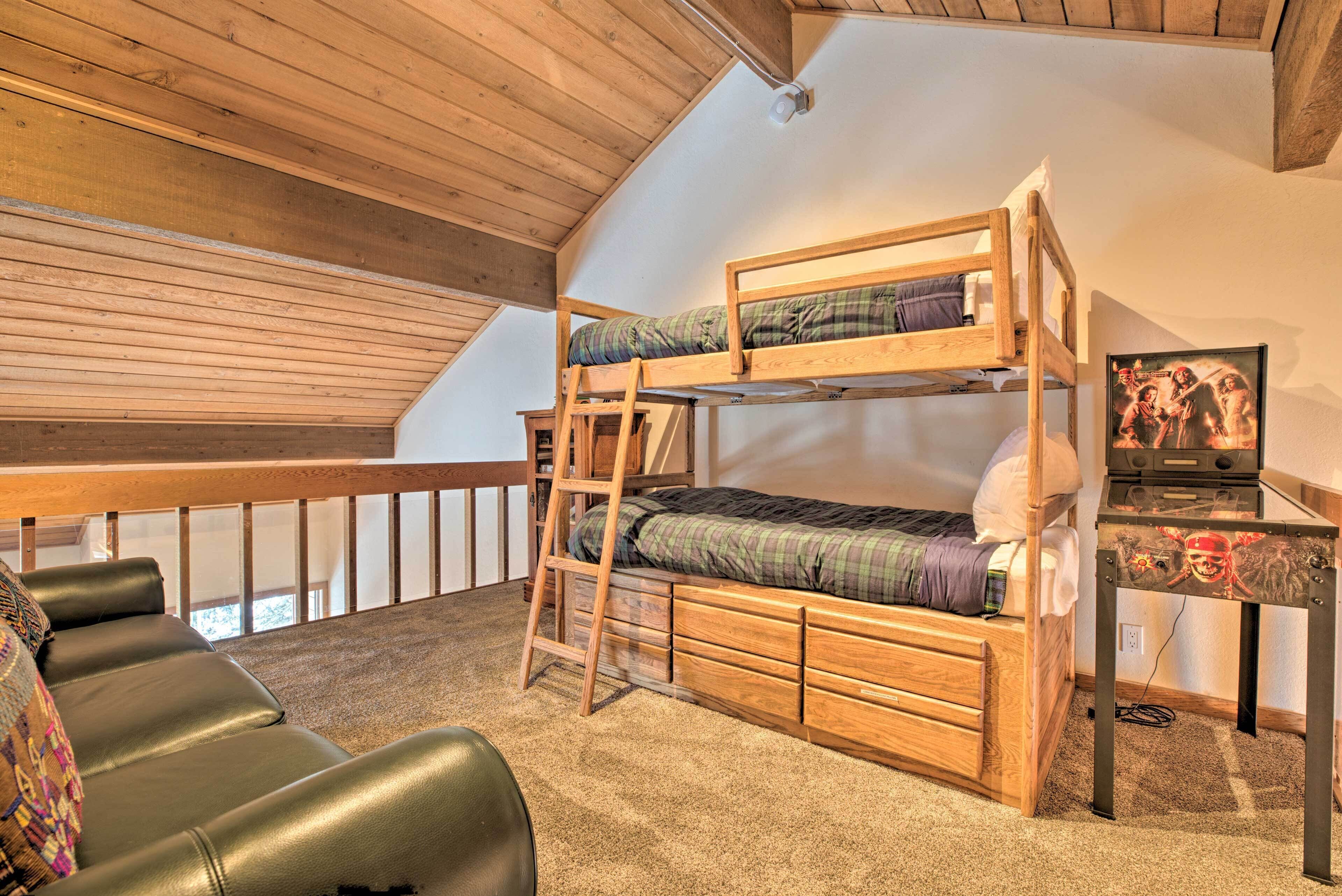 A bunk bed with a ladder, a desk with a computer, and a couch in a room with wooden beams and a sloped ceiling.