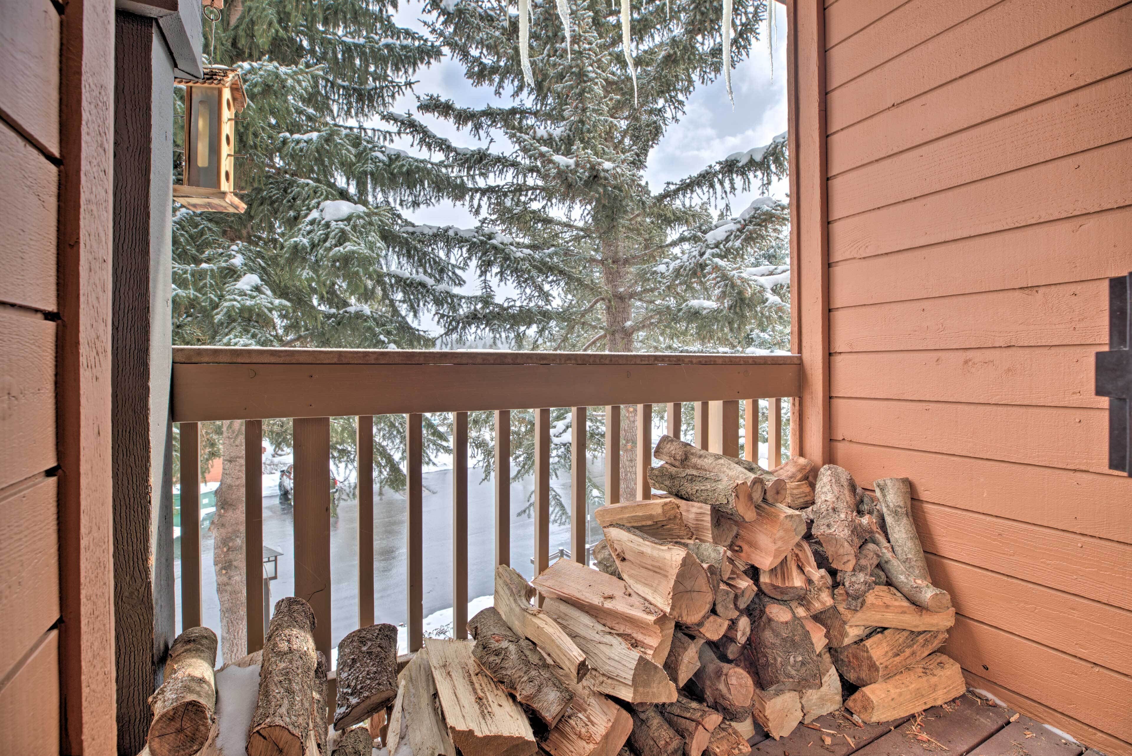 A wooden deck with a stack of firewood and a view of snow-covered trees.