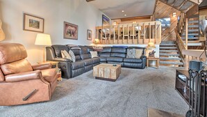 A spacious living room with a large sectional sofa, a leather armchair, and a wooden coffee table. A staircase with a wooden railing leads to an upper level. - The Mammoth Lodge by Hiking, Lakes, Skiing & More! (Mammoth Lakes)
