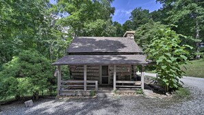A rustic log cabin with a porch, surrounded by lush greenery and a gravel driveway. - Historic Mountain Cabin: Grill & Hiking Trail! (Bryson City)
