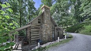 A rustic cabin with a stone chimney, a porch with outdoor seating, and a gravel driveway. - Historic Mountain Cabin: Grill & Hiking Trail! (Bryson City)