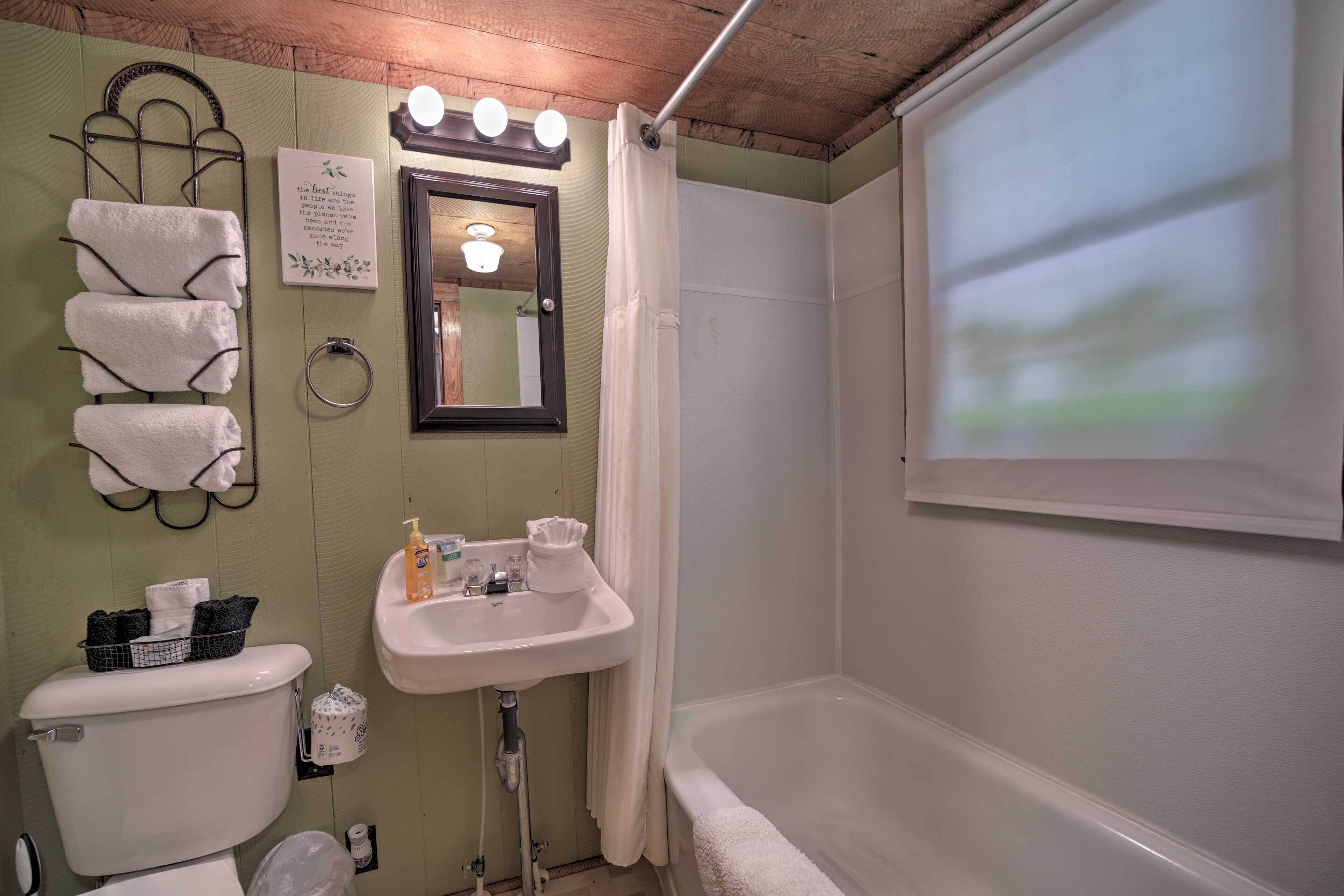 A bathroom with a toilet, sink, and bathtub. There are towels hanging on a rack, a mirror, and a window with a view.
