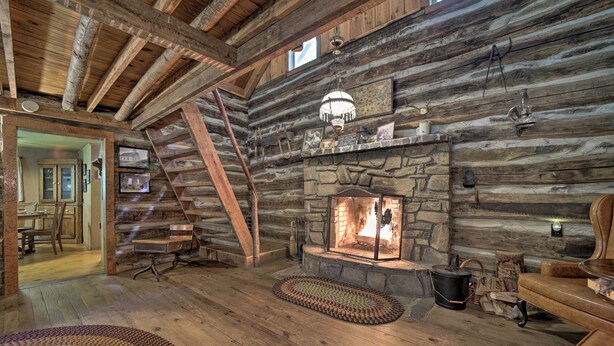 A rustic cabin interior with a stone fireplace, wooden beams, and a cozy seating area. - Historic Mountain Cabin: Grill & Hiking Trail! (Bryson City)