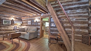 A log cabin interior with a wooden staircase, a sofa, a coffee table, and framed pictures on the walls. - Historic Mountain Cabin: Grill & Hiking Trail! (Bryson City)