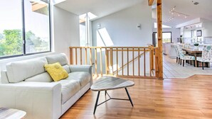 A spacious living area with a white leather sofa, a small wooden coffee table, and a dining area with patterned chairs. - Spacious Royal Oaks Retreat w/ Deck & Views! (Watsonville)