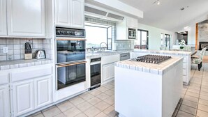 A modern kitchen with white cabinetry, a central island, built-in ovens, and a large window providing natural light. - Spacious Royal Oaks Retreat w/ Deck & Views! (Watsonville)