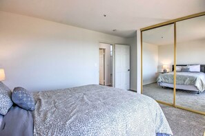 A bedroom with a large bed, a mirror, and a door leading to another room. - Spacious Royal Oaks Retreat w/ Deck & Views! (Watsonville)