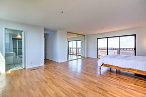Um quarto espaçoso com piso de madeira, uma cama grande, uma porta de vidro deslizante que dá para uma varanda e um guarda-roupa com espelho.