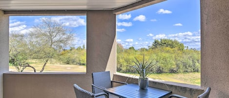 A covered patio area with wicker furniture and a table, overlooking a landscaped garden and trees.