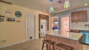 A kitchen with a central island, wooden bar stools, a refrigerator, and a dishwasher.