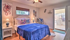 A bedroom with a bed, a ceiling fan, a window with blinds, a door leading to a balcony, and a wall with a decorative octopus painting.