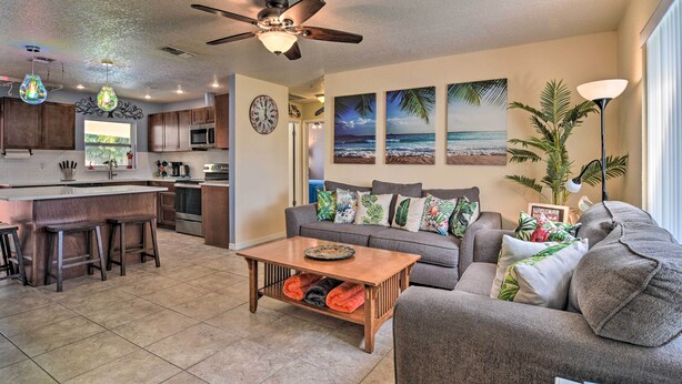 A modern living room with a gray sofa, a coffee table, and a kitchen area with wooden cabinets and a ceiling fan.