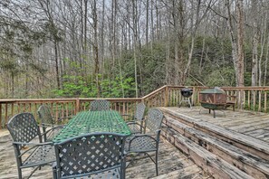Une terrasse en bois avec une table et des chaises en métal vert, entourée d’arbres.