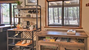 Una cocina con mostrador de madera, estantes con utensilios de cocina y vistas al bosque a través de una ventana.