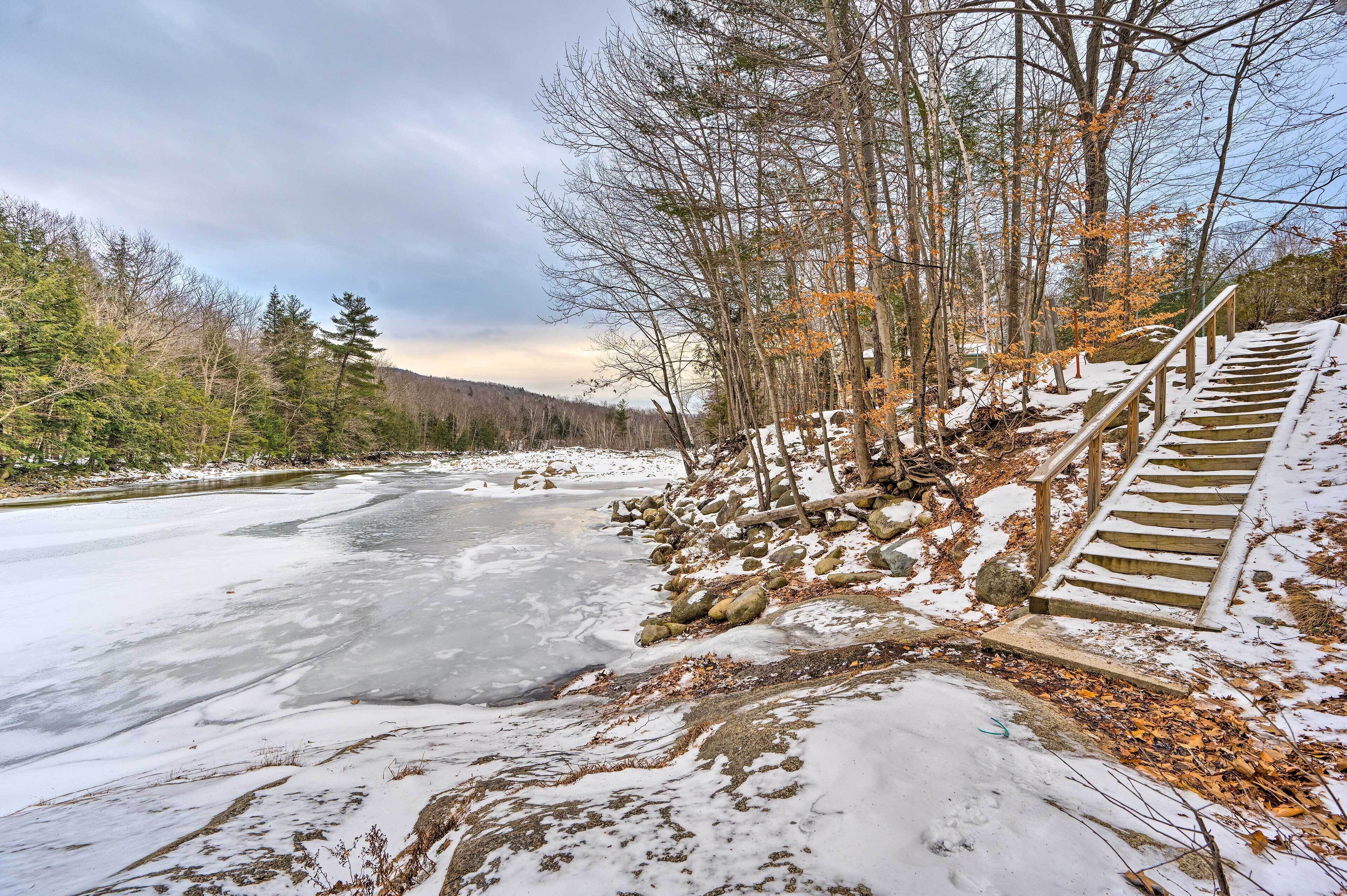 A snowy landscape with a frozen river, wooden stairs, and trees.
