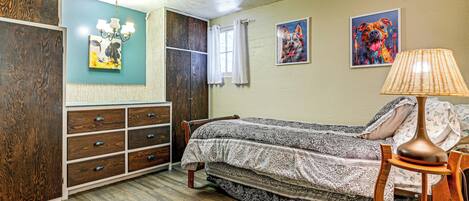 A bedroom with a bed, wooden dresser, and artwork on the wall.