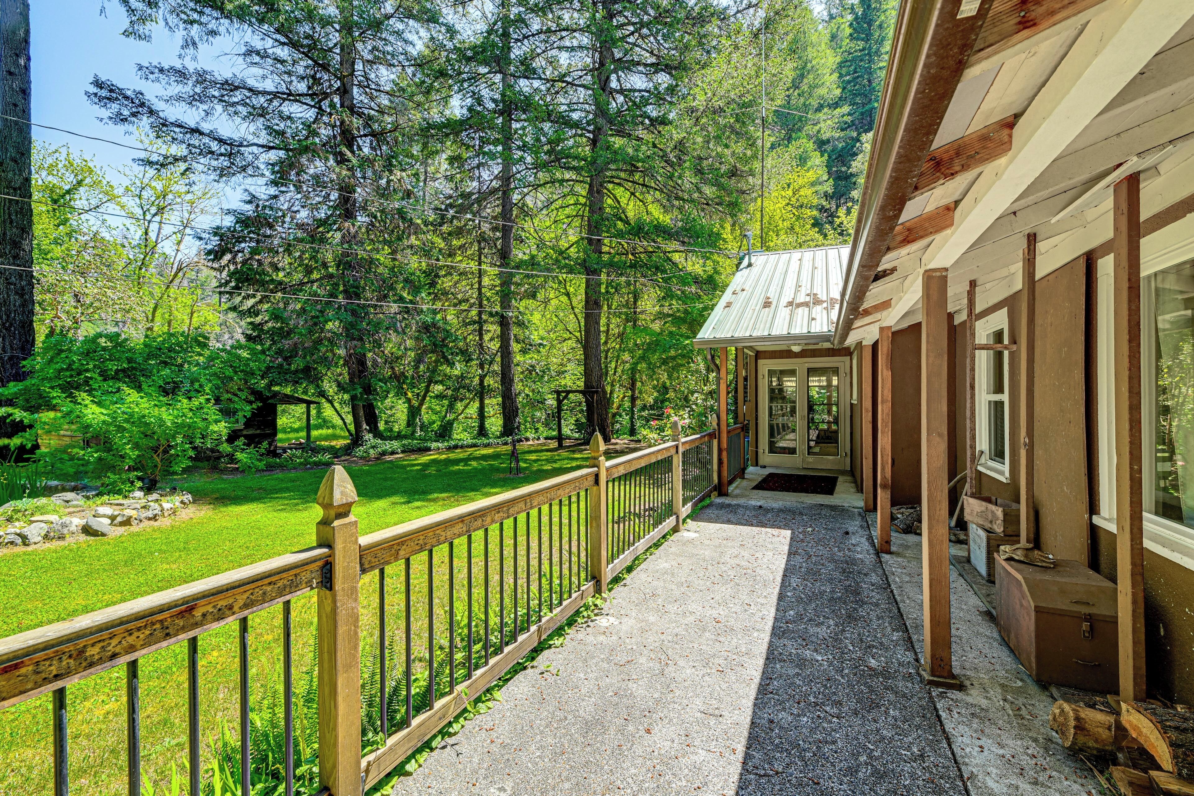 A wooden building with a porch, surrounded by a well-maintained garden and tall trees.