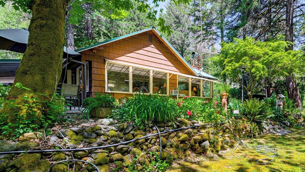 A rustic cabin with a sloped roof, surrounded by a lush garden with various plants and a small pond. - Outdoor Adventure: Tranquil Creekside Retreat (Merlin)