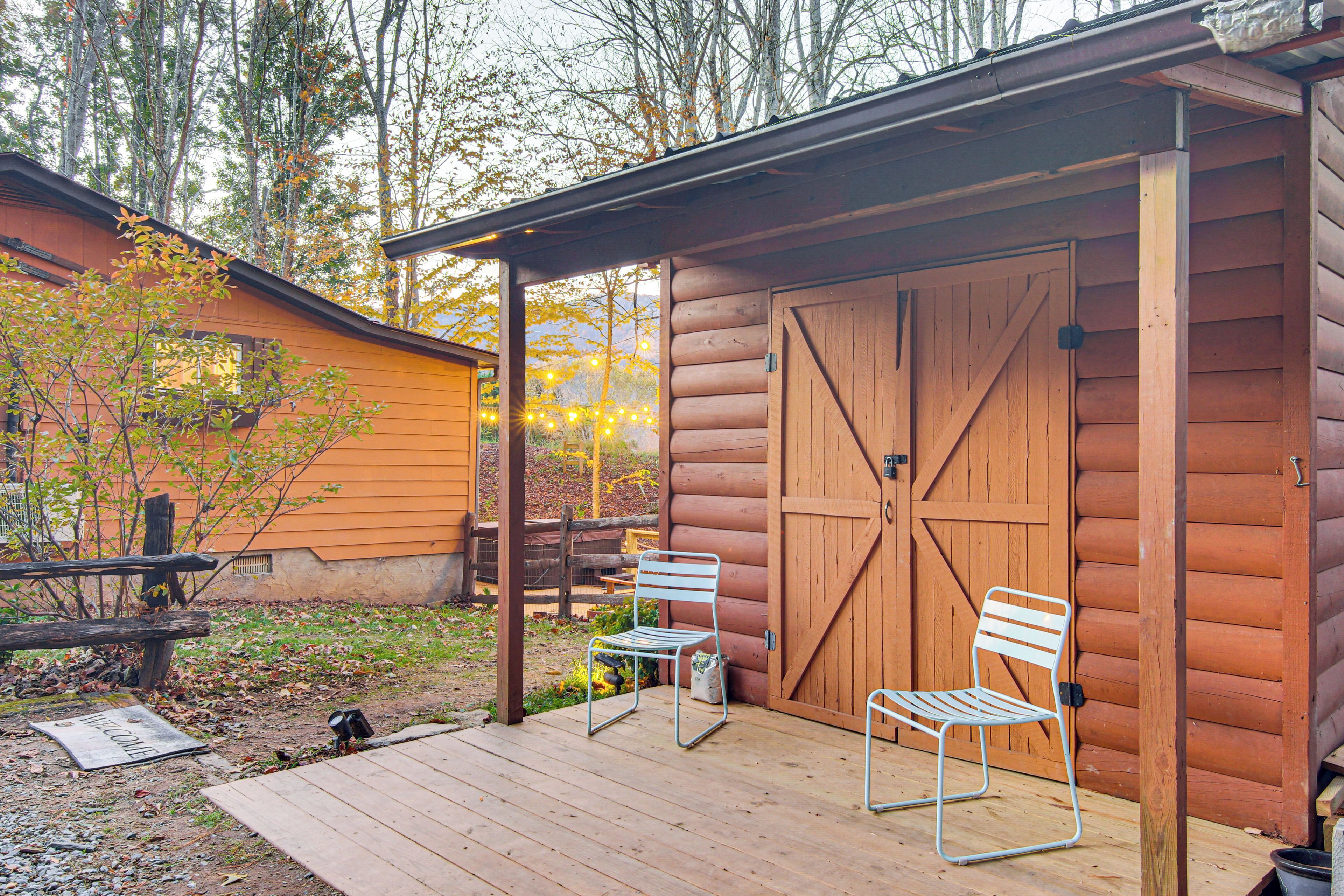 A wooden cabin with a porch, two metal chairs, and a wooden door.